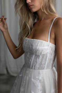 a woman with blonde hair wearing a white dress and holding her hand on her hip