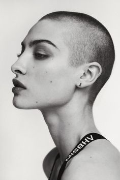 a black and white photo of a woman with shaved hair looking to the side while wearing a tank top