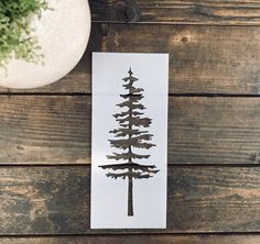 a card with a pine tree drawn on it next to a potted plant and wood planks