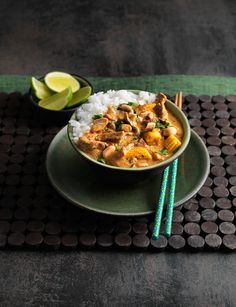 a green bowl filled with rice and meat next to chopsticks on a mat