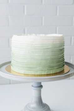 a frosted cake sitting on top of a white cake plate next to a brick wall