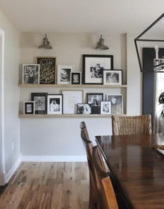 a dining room table with chairs and pictures on the wall above it, along with framed photos