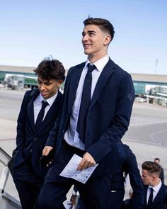 two men in suits are walking down the stairs at an airport while another man looks on