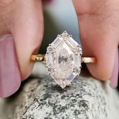 a woman's hand holding an engagement ring on top of a rock