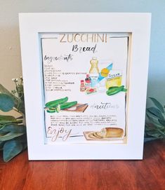 a picture frame with some bread and other items in it on a wooden table next to a potted plant