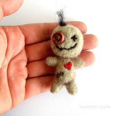 a hand holding a tiny stuffed animal in it's left hand, with a red heart on its nose