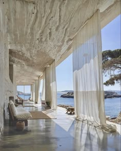 an empty room with sheer curtains on the walls and water in the background, along with two chaise lounges