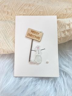 a card with a snowman holding a wooden sign that says merry christmas on it