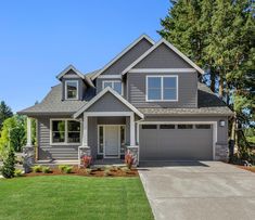 a large gray house with two garages in the front yard and trees behind it