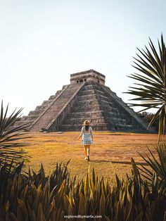 a woman walking across a grass covered field next to a tall pyramid in the background