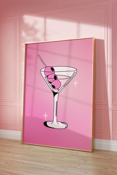 a pink poster with a martini glass and olives on the rim in front of a pink wall