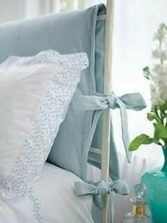 a blue vase with flowers on the side of a bed next to a white pillow