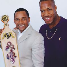 two men holding up a skateboard with pictures on it