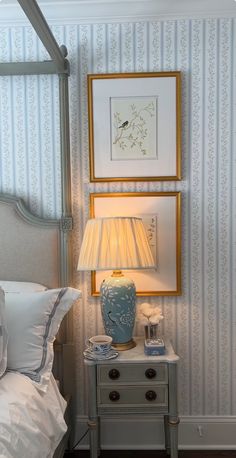 a bedroom with blue and white striped wallpaper, a lamp on the nightstand and pictures above it