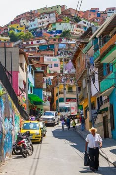 a woman walking down a street next to tall buildings with graffiti on the side of it