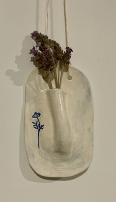 a ceramic vase with flowers in it hanging from a rope on the wall next to a white wall