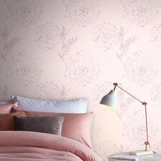 a bed with pink sheets and pillows next to a lamp