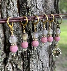 five pairs of pink and gold earrings hanging from a hook on a wooden tree branch