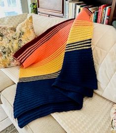 a multicolored blanket is laying on the back of a couch in front of a bookcase