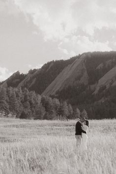 a man and woman standing in a field with mountains in the backgrouds