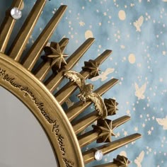 an ornate mirror with gold stars and birds on the wall next to it is sitting against a blue background