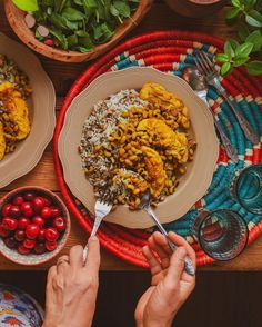 two people eating food from plates on a table with bowls of cherries and other foods