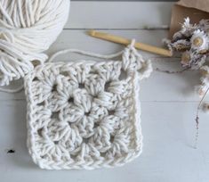 a white crochet square next to a ball of yarn