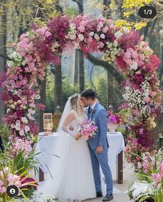 a bride and groom standing in front of a floral arch at their outdoor wedding ceremony