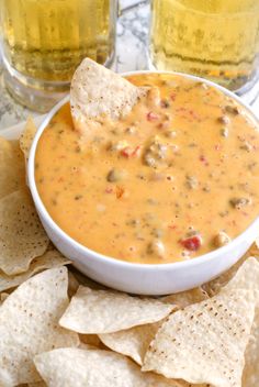 a white bowl filled with cheese dip surrounded by tortilla chips