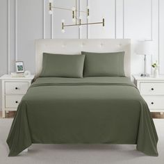 a bed with green sheets and pillows in a white room next to two nightstands