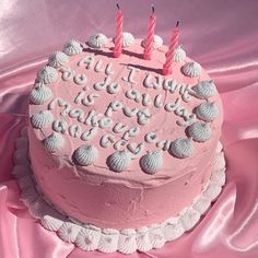 a pink birthday cake with seashells on it and candles in the shape of letters