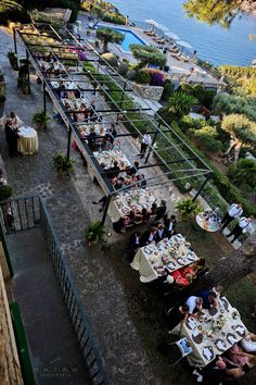 a group of people sitting at tables in the middle of a park next to water