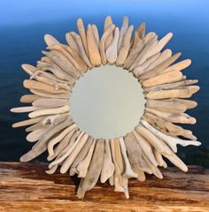 a mirror made out of driftwood sitting on top of a wooden table next to the ocean