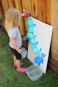 two young children playing with toys in the grass near a wooden wall and fenced area