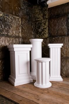 three white pedestals sitting on top of a wooden floor in front of a wall