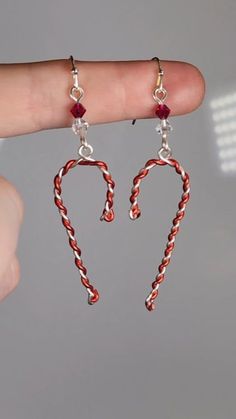 a pair of red and white candy canes dangling from earrings on someone's finger