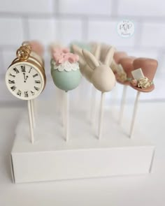 four cake pops with different types of decorations on top of them, and one has a clock in the middle