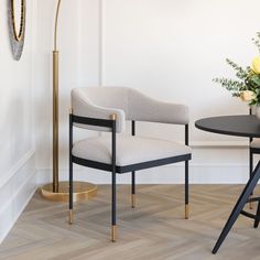 a white chair sitting next to a black table with flowers on it and a gold floor lamp