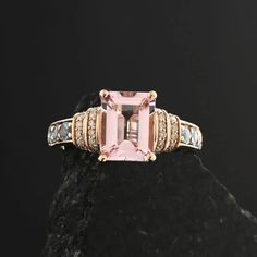 a pink tourmaline and diamond ring sitting on top of a black stone slab