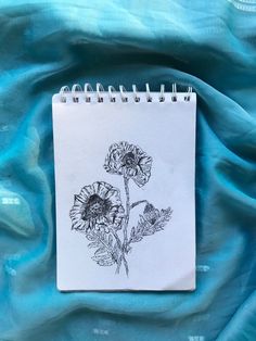 a notebook with a drawing of sunflowers on it sitting on a blue cloth