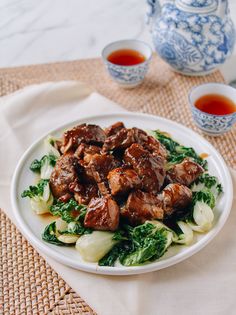 a white plate topped with meat and veggies next to two cups of tea