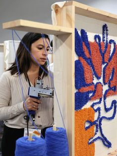 a woman working on an art project with blue and orange yarn in front of her