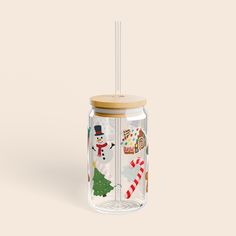 a glass jar with a straw in it and christmas decorations on the lid, next to a wooden stick