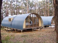 a couple of small houses in the middle of a forest with trees around them and one is made out of wood