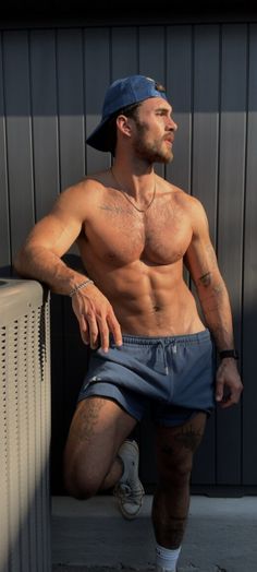 a shirtless man leaning against a wall with his hands on his hips and looking off to the side