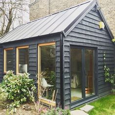 a small black house with lots of windows and plants in the front garden area,