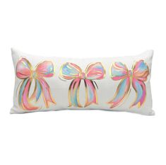 a white pillow with pink bows on the front and blue, green, yellow, and pink ribbons on the back