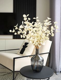 a glass vase with white flowers on a table in front of a couch and television