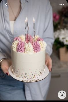 a woman holding a white cake with pink and white flowers on it that says happy birthday