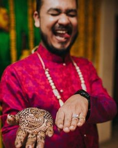 a man in a red shirt is holding a henna on his hand and smiling